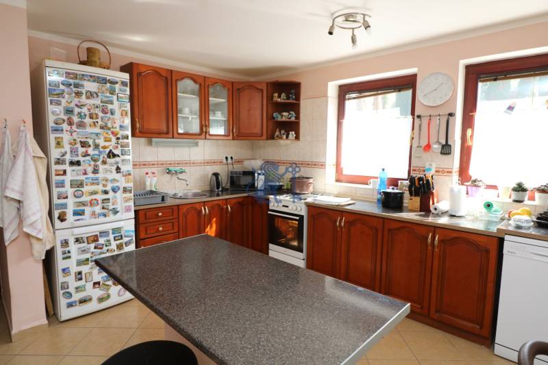 ZNÍŽENÁ cena - viacgeneračný  rodinný dom v Borinke  - Kuchyňa s drevenými skrinkami, spotrebičmi a stolom na ulici Borinka v rodinnom dome.