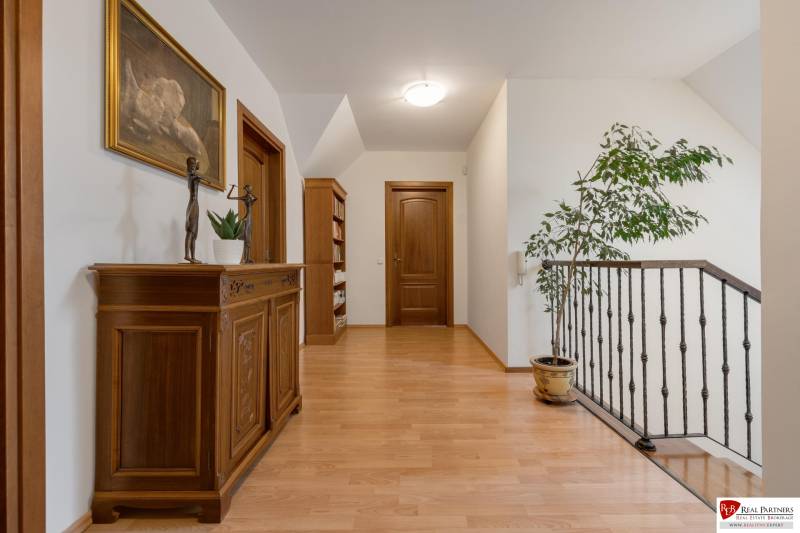 Predaj luxusná 5 izbová Vila,440 m2,pozemok 1061m2,garáž,bazén. - Chodba s dreveným nábytkom, knihovňa, sochy na ulici Hrušovská, schodisko vo vile, rastlina.