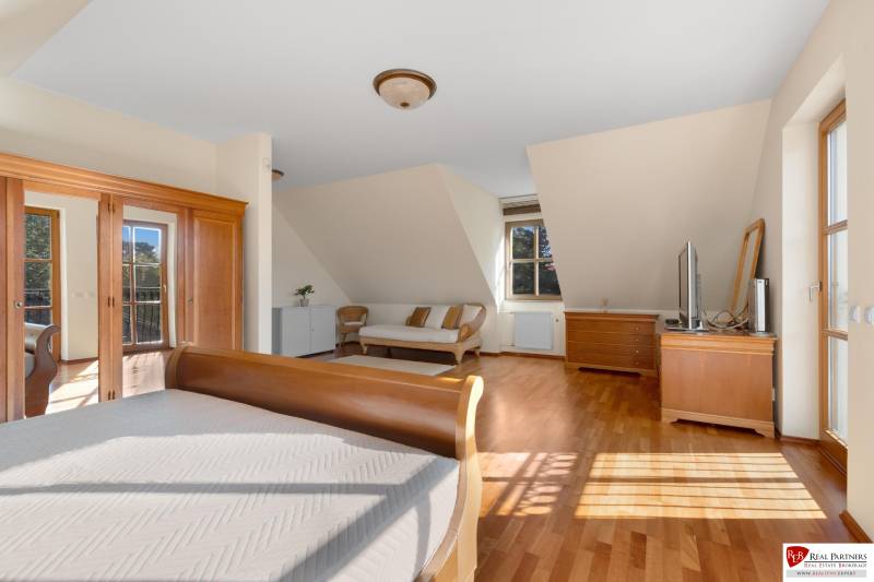 Predaj luxusná 5 izbová Vila,440 m2,pozemok 1061m2,garáž,bazén. - Priestranná spálňa s drevenou podlahou na ulici Hrušovská, obsahujúca nábytok a televízor pri vile.