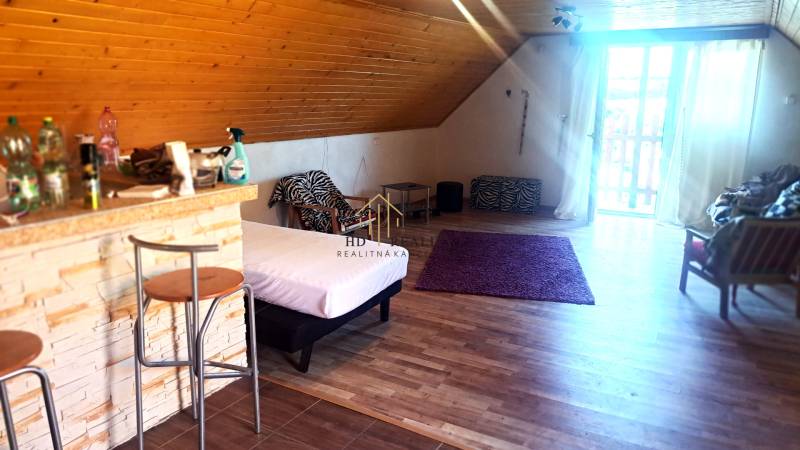 Predaj chaty a chalupy, Levice - Interiér chaty s barovým pultom, posteľou a podlahou s dreveným dekorom.