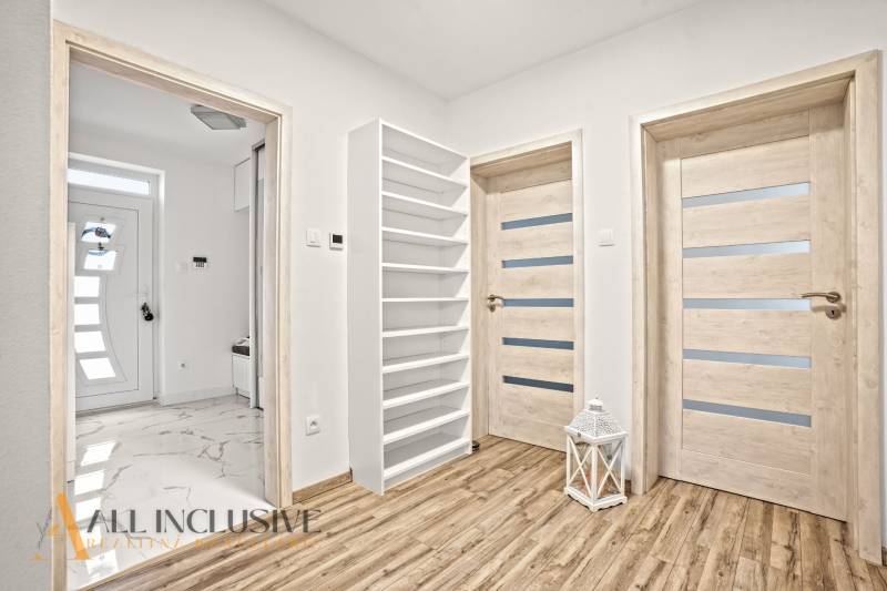 NA PREDAJ MODERNÝ 3-IZB. RD TYPU BUNGALOV V GABČÍKOVE - Interiér rodinného domu s podlahou s dreveným dekorom, dverami a bielym regálom.