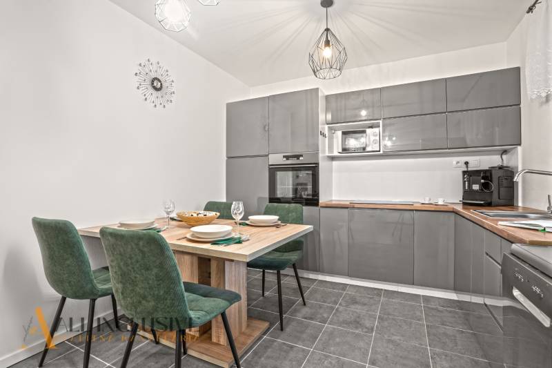 NA PREDAJ MODERNÝ 3-IZB. RD TYPU BUNGALOV V GABČÍKOVE - Kuchyňa v rodinnom dome so sivou linkou, jedálenským stolom a zelenými stoličkami.