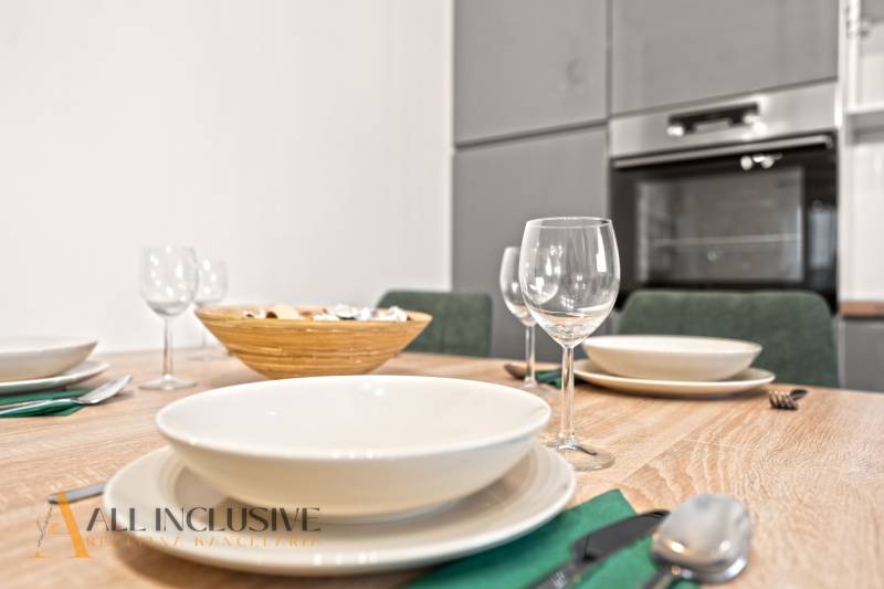 NA PREDAJ MODERNÝ 3-IZB. RD TYPU BUNGALOV V GABČÍKOVE - Jedálenský stôl so stolovaním a pohármi, v pozadí kuchyňa v rodinnom dome.