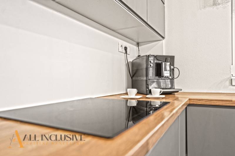 NA PREDAJ MODERNÝ 3-IZB. RD TYPU BUNGALOV V GABČÍKOVE - Kuchyňa v rodinnom dome s kávovarom a varnou doskou na drevenom dekore.