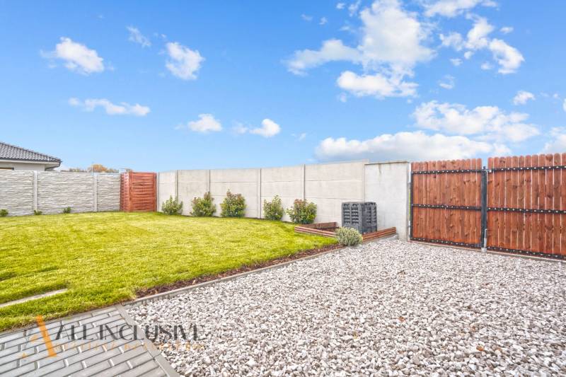 NA PREDAJ MODERNÝ 3-IZB. RD TYPU BUNGALOV V GABČÍKOVE - Záhrada pri rodinnom dome v Gabčíkove s trávnikom, kamienkami a dreveným plotom.