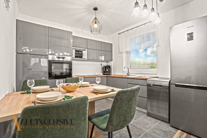 NA PREDAJ MODERNÝ 3-IZB. RD TYPU BUNGALOV V GABČÍKOVE - Moderná kuchyňa v rodinnom dome s dreveným dekorom stola a viacerými spotrebičmi.