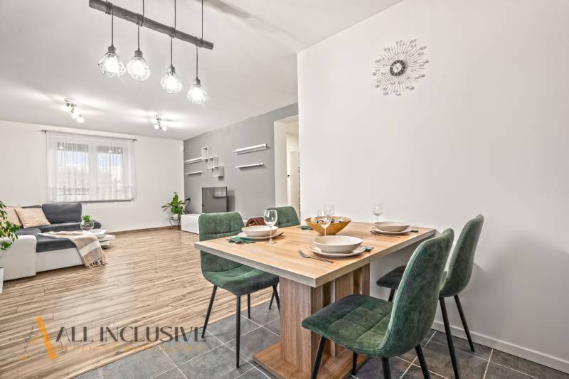 NA PREDAJ MODERNÝ 3-IZB. RD TYPU BUNGALOV V GABČÍKOVE - Interiér rodinného domu s podlahou s dreveným dekorom, jedálenský stôl a zelené stoličky.