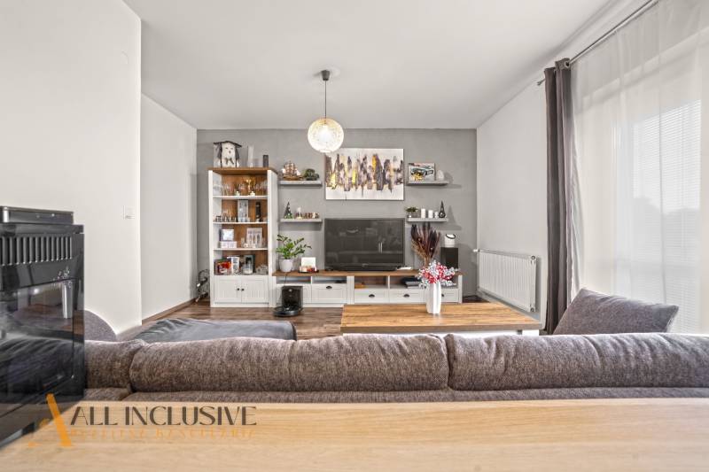 NA PREDAJ 2-IZBOVÝ BYT S 2 BALKÓNMI, DUNAJSKÁ STREDA - Obývačka v 2-izbovom byte s podlahou s dreveným dekorom a veľkou sedačkou.