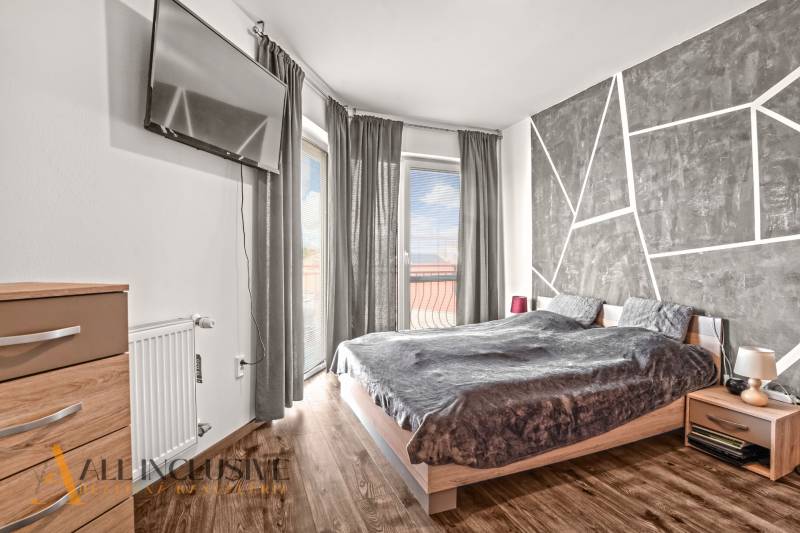 NA PREDAJ 2-IZBOVÝ BYT S 2 BALKÓNMI, DUNAJSKÁ STREDA - Spálňa v 2-izbovom byte s televízorom, posteľou a podlahou s dreveným dekorom.