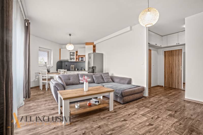 NA PREDAJ 2-IZBOVÝ BYT S 2 BALKÓNMI, DUNAJSKÁ STREDA - Obývacia izba 2-izbového bytu s pohovkou a podlahou s dreveným dekorom.