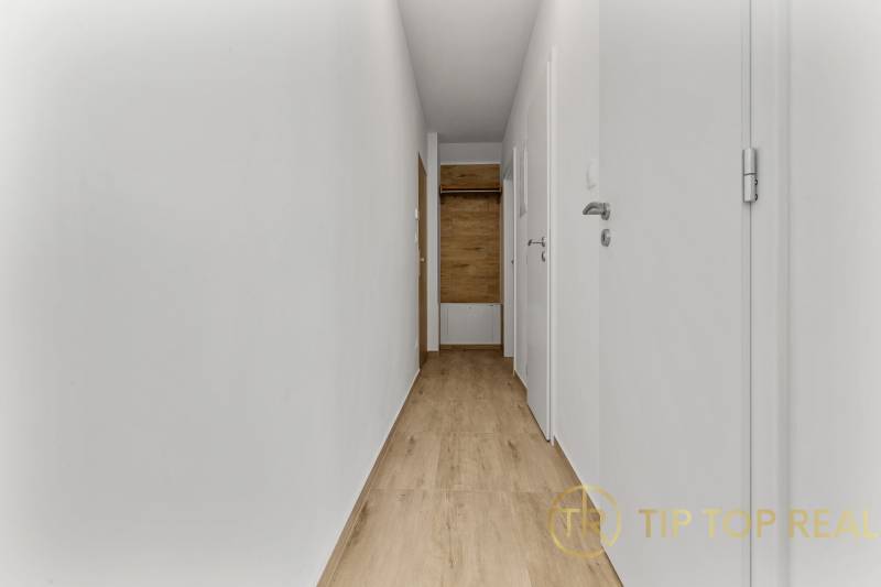 OPAL - NOVÝ a KOMPLETNE ZARIADENÝ 2,5-izbový byt s LODŽIOU a PARKOVANÍ - Úzka chodba so stenami v 2-izbovom byte, podlaha s dreveným dekorom, svetlé dvere.