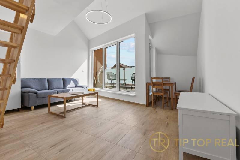 OPAL - NOVÝ a KOMPLETNE ZARIADENÝ 2,5-izbový byt s LODŽIOU a PARKOVANÍ - Obývačka v 2-izbovom byte s podlahou s dreveným dekorom, gaučom a balkónom.