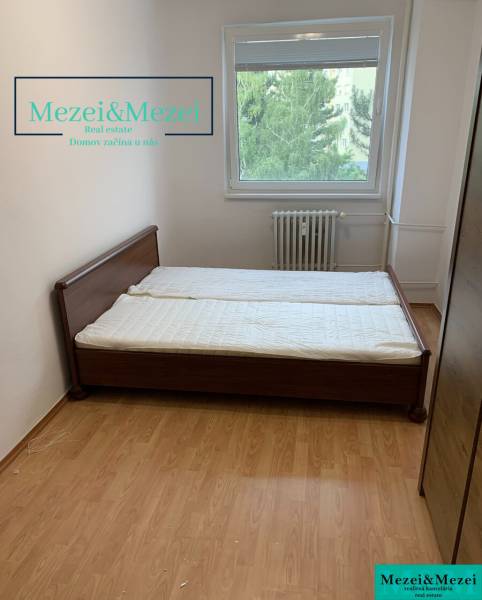 Na predaj prakticky riešený 2-izbový byt s balkónom - Spálňa s posteľou, podlaha s dreveným dekorom, okno s výhľadom na zeleň.