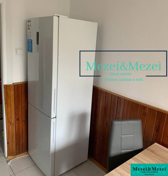 Na predaj prakticky riešený 2-izbový byt s balkónom - Kuchyňa v 2-izbovom byte, chladnička, drevený obklad, šedá stolička, jedálenský stôl.