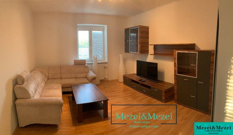 Na predaj útulný 2-izbový byt, Bratislava – Nové Mesto - Obývacia izba s béžovou sedačkou, dreveným nábytkom a podlahou s dreveným dekorom.