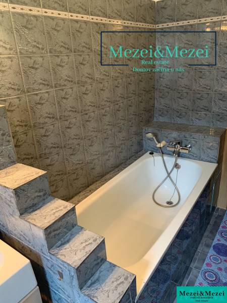 Na predaj útulný 2-izbový byt, Bratislava – Nové Mesto - Kúpeľňa so schodíkmi a vaňou obklopená sivými obkladmi v 2-izbovom byte.