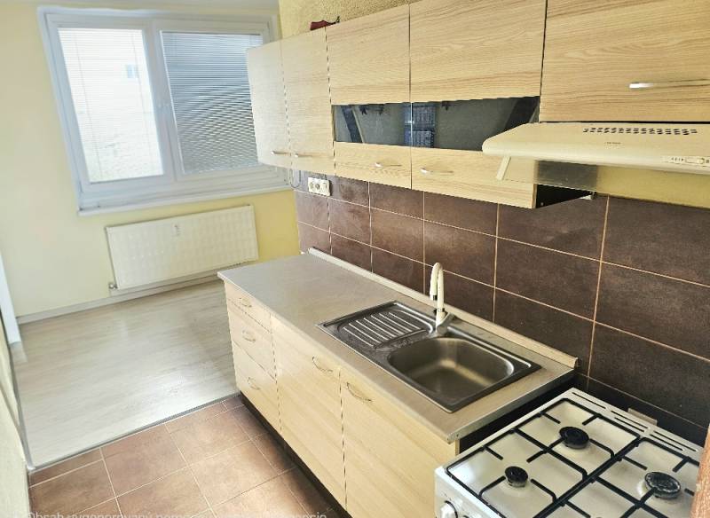2,5 izbový byt Bánovce nad Bebravou/CENTRUM- STRED/KOMLETNÁ REKONŠTRUK - Kuchyňa v 2-izbovom byte s bielymi skrinkami a podlahou s dreveným dekorom.