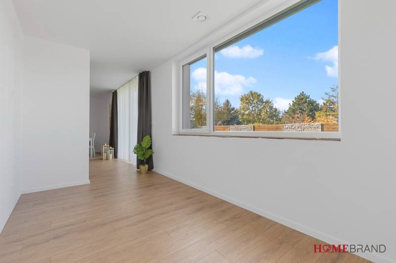 BÝVANIE VO VILA DOME - POSLEDNÝ VOĽNÝ 3-IZBOVÝ BYT SO ZÁHRADOU - Biely interiér s veľkými oknami a podlahou s dreveným dekorom v 3-izbovom byte.