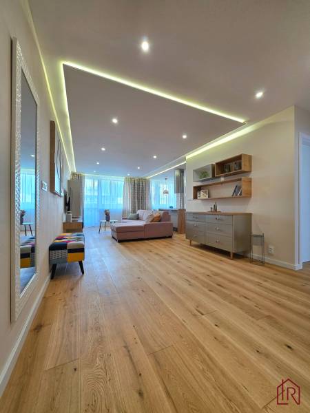 REZERVOVANÉ - 3i, OV, 71m2 + loggia, Lomonosovova, dizajnový, zariaden - Obývacia izba s podlahou s dreveným dekorom v 3-izbovom byte, pohodlnou sedačkou a dekoráciami.