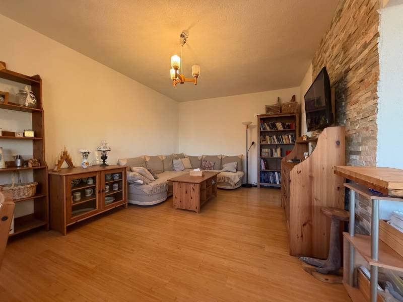 - PREDAJ - 2 izbový byt - Astrová ul. - Ružinov - Obývacia izba s pohovkou, podlaha s dreveným dekorom, knižnica a televízor na stene.