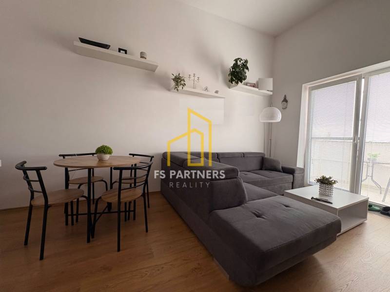 Prenájom moderného 2-izbového bytu v centre Komárna, 40 m² – Petőfiho  - Obývacia izba s tmavosivou pohovkou a podlahou s dreveným dekorom v 2-izbovom byte.