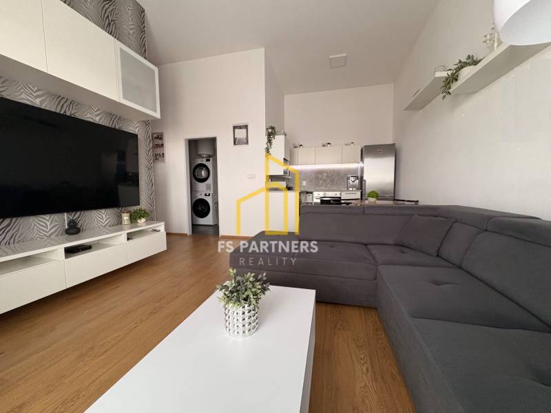 Prenájom moderného 2-izbového bytu v centre Komárna, 40 m² – Petőfiho  - Obývacia izba s veľkou sedačkou, podlahou s dreveným dekorom a televízorom v 2-izbovom byte.