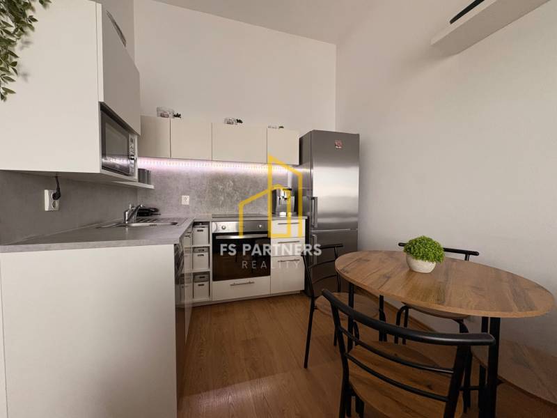 Prenájom moderného 2-izbového bytu v centre Komárna, 40 m² – Petőfiho  - Kuchyňa v 2-izbovom byte s podlahou s dreveným dekorom a jedálenským stolom.