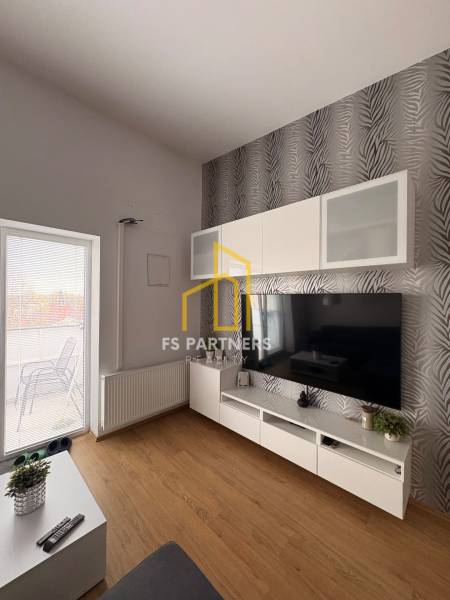 Prenájom moderného 2-izbového bytu v centre Komárna, 40 m² – Petőfiho  - Obývacia izba s TV stenou, vzorovanou tapetou a podlahou s dreveným dekorom v 2-izbovom byte.