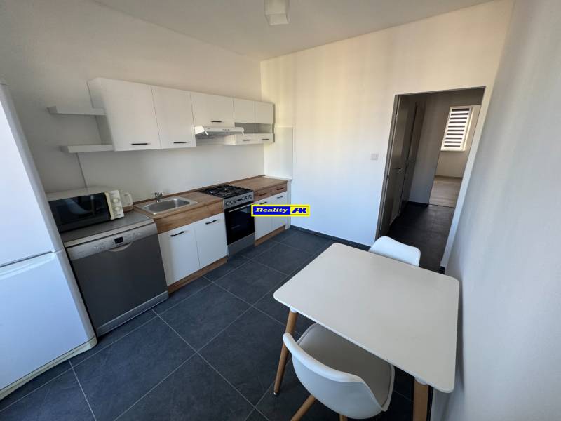 3 izbový zrekonštruovaný byt na prenájom - Martin - Kuchyňa v 3-izbovom byte s bielymi skrinkami a stolom, na tmavej podlahe.