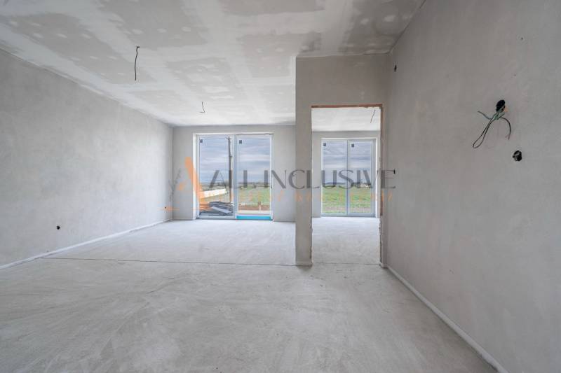 ALL INCLUSIVE I 3 IZBOVÉ BYTY S TERASOU, SO ZÁHRADOU + 2 PARK. MIESTA - Nedokončený interiér 3-izbového bytu s omietnutými stenami a veľkými oknami.