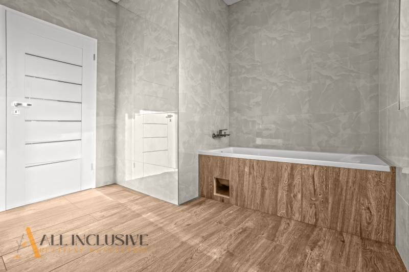 ALL INCLUSIVE I 3 IZBOVÉ BYTY S TERASOU, SO ZÁHRADOU + 2 PARK. MIESTA - Kúpeľňa v 3-izbovom byte s podlahou s dreveným dekorom, vaňou a bielymi dverami.