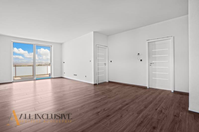 ALL INCLUSIVE I 3 IZBOVÉ BYTY S TERASOU, SO ZÁHRADOU + 2 PARK. MIESTA - Priestranný interiér 3-izbového bytu s podlahou s dreveným dekorom a výhľadom z okna.