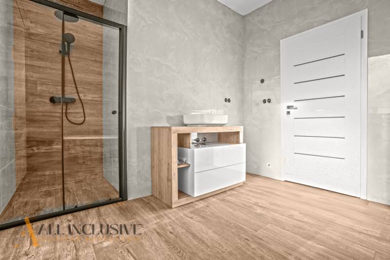 ALL INCLUSIVE I 3 IZBOVÉ BYTY S TERASOU, SO ZÁHRADOU + 2 PARK. MIESTA - Kúpeľňa v 3-izbovom byte s podlahou s dreveným dekorom, skleneným sprchovým kútom a modernou sanitou.