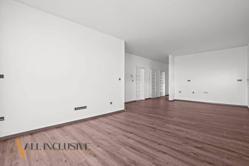 ALL INCLUSIVE I 3 IZBOVÉ BYTY S TERASOU, SO ZÁHRADOU + 2 PARK. MIESTA - Priestranný interiér 3-izbového bytu s podlahou s dreveným dekorom a bielymi stenami.