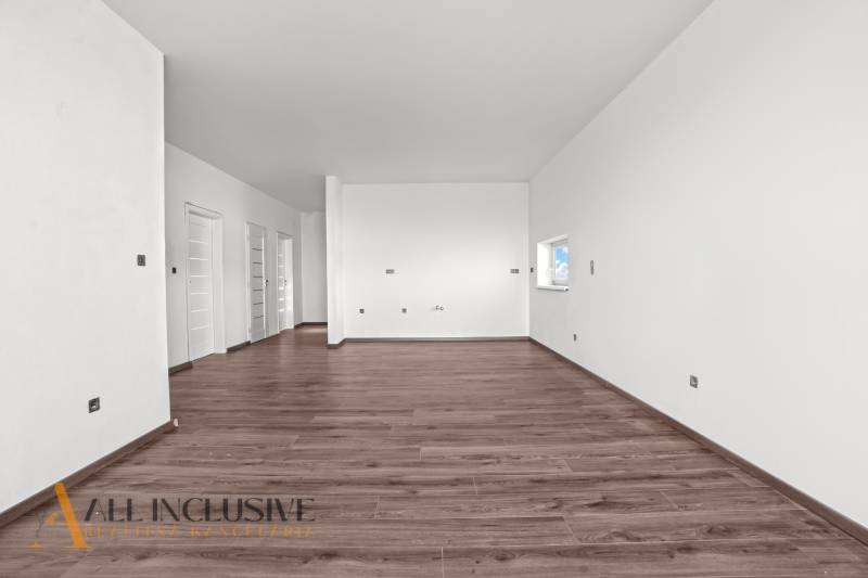 ALL INCLUSIVE I 3 IZBOVÉ BYTY S TERASOU, SO ZÁHRADOU + 2 PARK. MIESTA - Priestranná miestnosť v 3-izbovom byte s bielymi stenami a podlahou s dreveným dekorom.