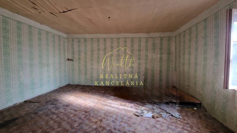 Vidiecky dom v Zemplínskej Teplici - Izba v rodinnom dome s poškodeným stropom, tapetami a podlahou s dreveným dekorom.