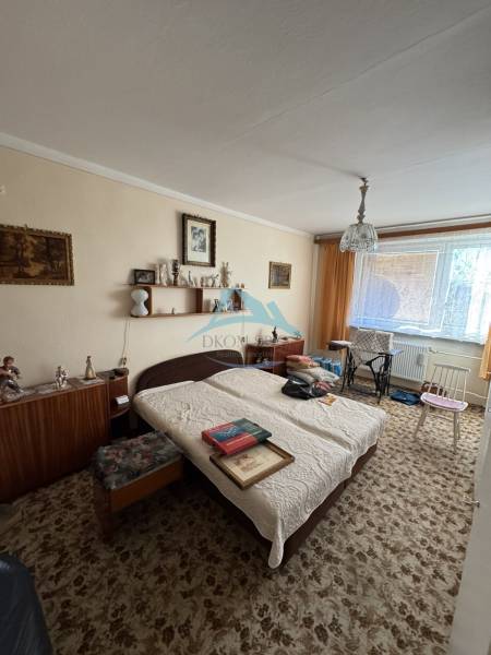 Šahy – 3i Byt v Centre Mesta s Balkónom  - Izba v 3-izbovom byte s postieľkou, kobercom a nábytkom, dekorácie na stenách.