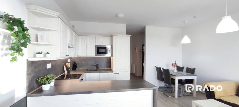 | 2-izbový byt, ul. Predmerského VINOHRADY | Trenčín  - Kuchyňa 2-izbového bytu s bielymi skrinkami a jedálenským stolom, podlaha s dreveným dekorom.