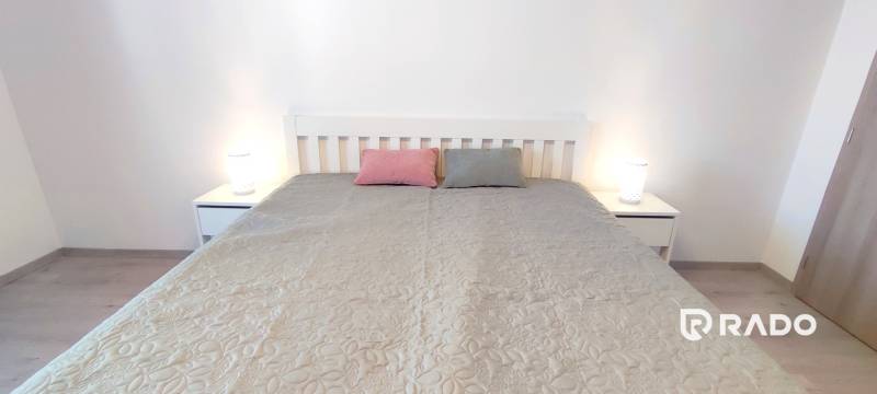 | 2-izbový byt, ul. Predmerského VINOHRADY | Trenčín  - Spálňa s posteľou, dvoma vankúšmi a nočnými stolíkmi v 2-izbovom byte.