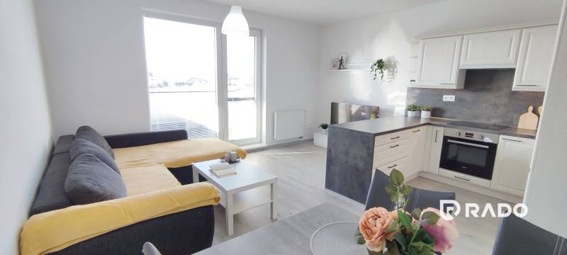 | 2-izbový byt, ul. Predmerského VINOHRADY | Trenčín  - Interiér 2-izbového bytu s kuchyňou, pohovkou a podlahou s dreveným dekorom.