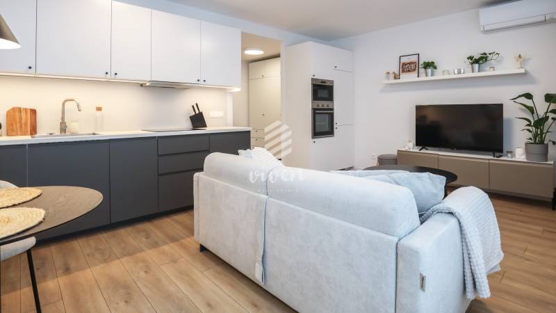 PRENÁJOM - 1 izbový byt v projekte Ovocné sady - Obývačka 1-izbového bytu s kuchynskou linkou, gaučom a podlahou s dreveným dekorom.