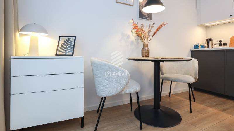 PRENÁJOM - 1 izbový byt v projekte Ovocné sady - 1-izbový byt s dekoratívnymi stoličkami, stolom a lampou na podlahe s dreveným dekorom.