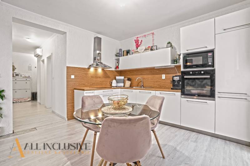 NA PREDAJ 3-IZB. BYT S TERASOU A ZÁHRADKOU, DUN.STREDA - Kuchyňa v 3-izbovom byte s bielymi skrinkami, podlahou s dreveným dekorom a jedálenským stolom.