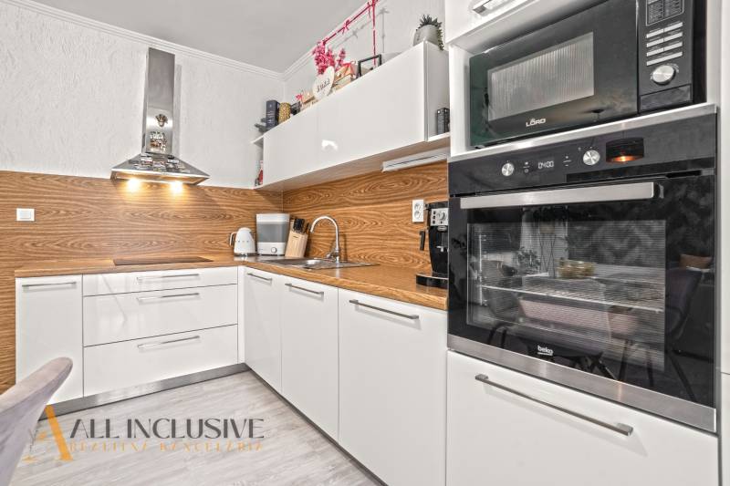 NA PREDAJ 3-IZB. BYT S TERASOU A ZÁHRADKOU, DUN.STREDA - Moderná kuchyňa v 3-izbovom byte s bielymi skrinkami a podlahou s dreveným dekorom.