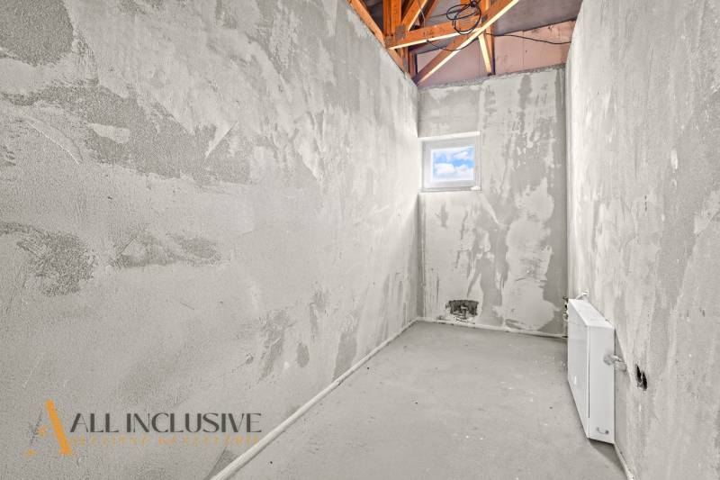 NA PREDAJ 4-IZBOVÝ RD - NOVOSTAVBA, DUNAJSKÁ STREDA  - Nedokončená miestnosť, na stenách sivá omietka, s malým oknom a viditeľnou strešnou konštrukciou.