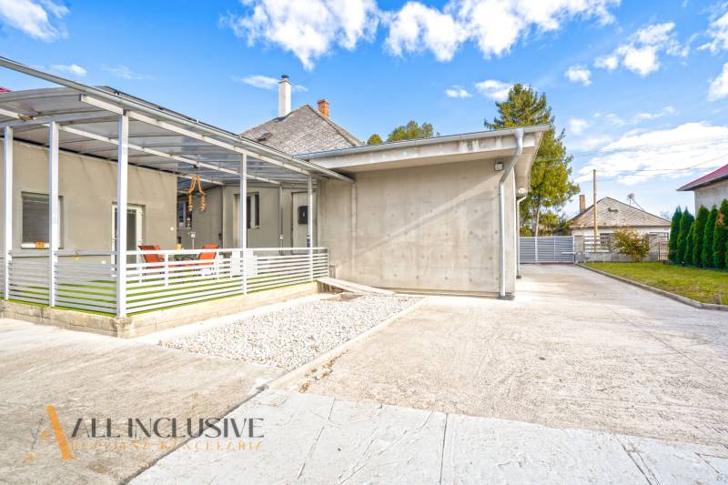 NA PREDAJ 4+1-IZBOVÝ ROD. DOM, VEĽKÉ KOSIHY - Rodinný dom vo Veľkých Kosihách: betónová terasa, prístrešok, záhrada, modrá obloha.