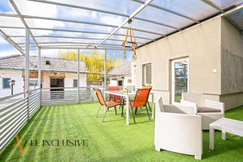 NA PREDAJ 4+1-IZBOVÝ ROD. DOM, VEĽKÉ KOSIHY - Terasa rodinného domu vo Veľkých Kosihách s presklenou strechou a nábytkom na umelej tráve.