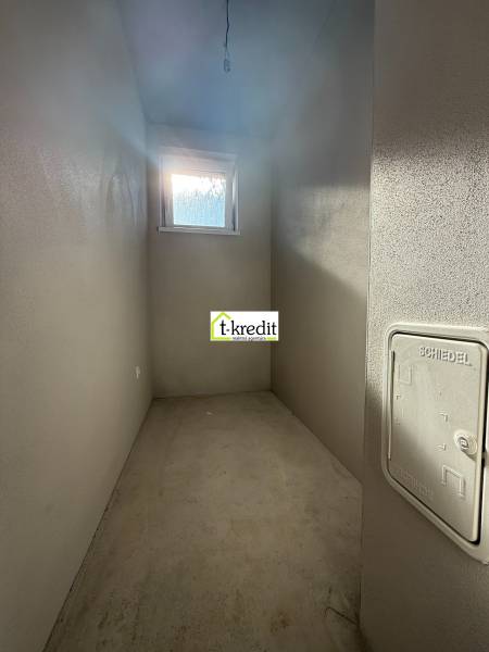 PREDAJ - NOVOSTAVBA - TESÁRSKE MLYŇANY - Úzka úložná miestnosť v rodinnom dome s oknom a betónovou podlahou.