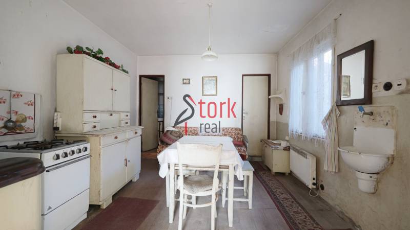 Menší rodinný dom len pár metrov od centra mesta Rajec - Kuchyňa v rodinnom dome s retro nábytkom, stolom a umývadlom, podlaha s dreveným dekorom.