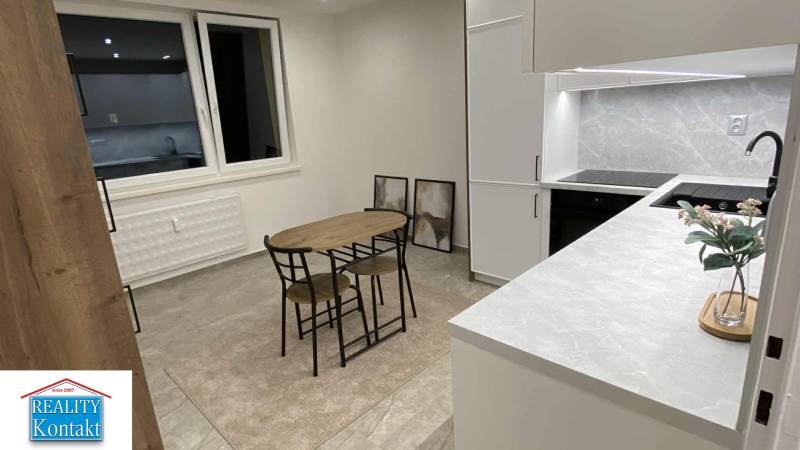 Na prenájom 1-izbový byt - Nové Zámky - Kuchyňa v 1-izbovom byte s jedálenským stolom, skriňami a dekoračnými obrazmi na stene.